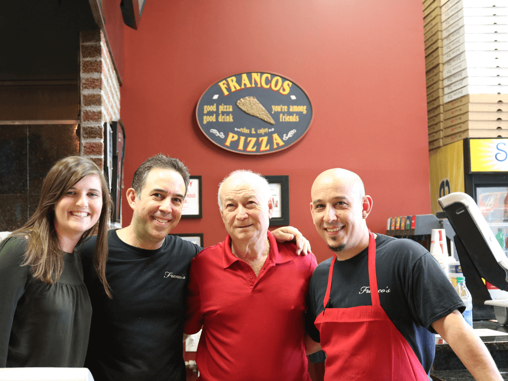 Four people standing in front of a Franco's Pizza sign