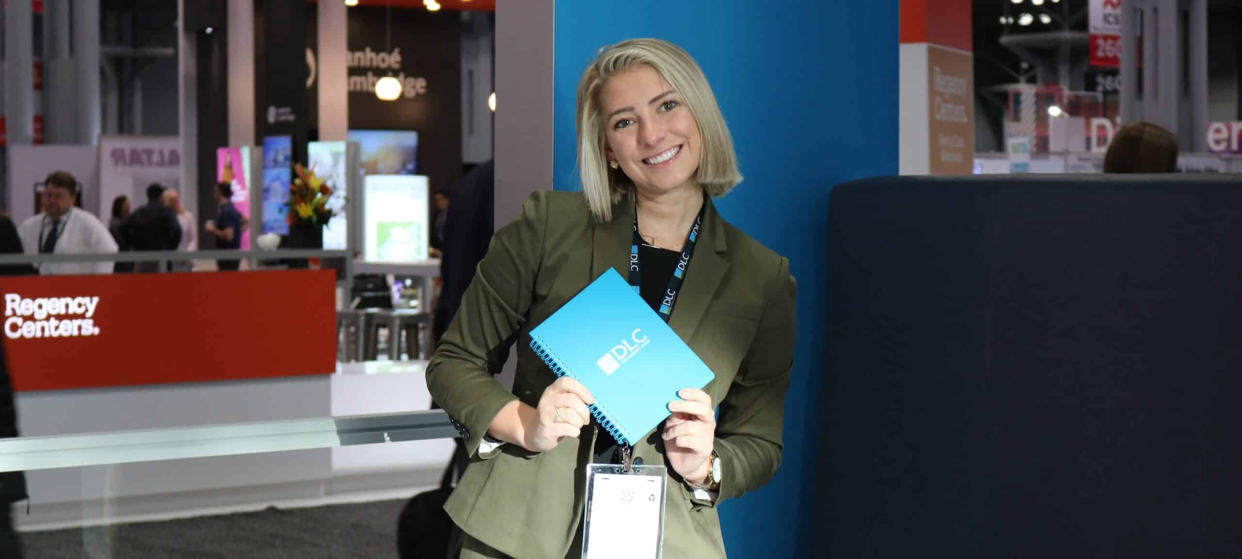 A woman smiling while holding up a DLC notebook