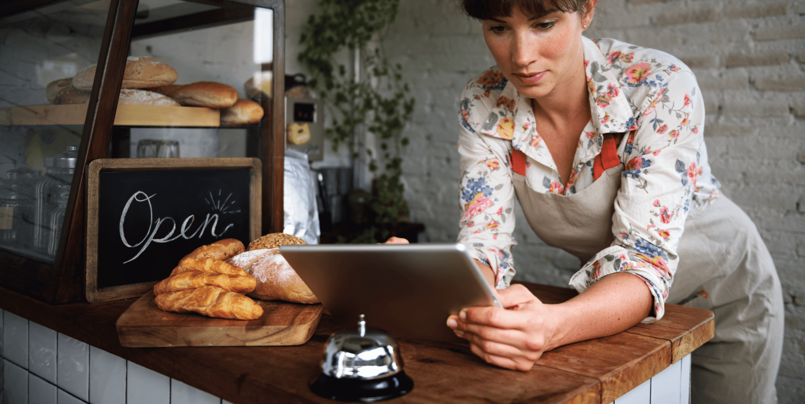 A woman standing at a bakery counter looking at an ipad