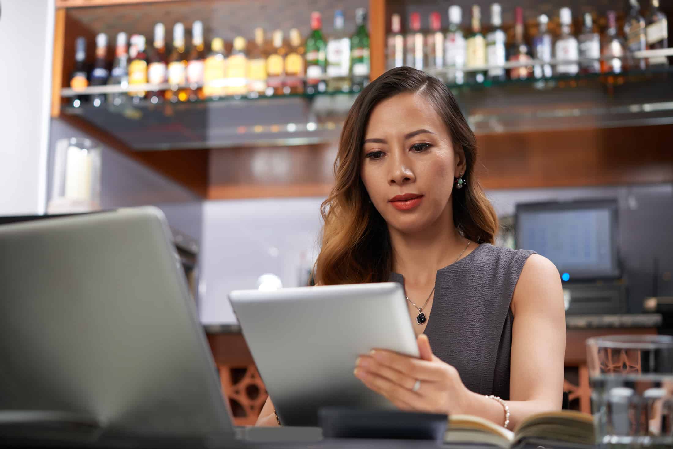 Woman standing behind a bar looking at an ipad